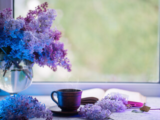 Wall Mural - Spring still life with a cup of coffee and bouquets of lilacs. Colored light. Reading a book and drinking coffee by the window, spring mood