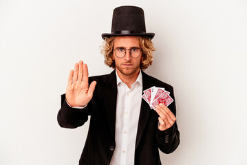 Wall Mural - Young magician caucasian man holding magic cards isolated on white background standing with outstretched hand showing stop sign, preventing you.