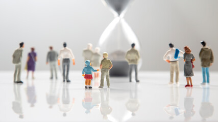 miniature people. different people are walking next to the hourglass on a white background. lifespan of humanity