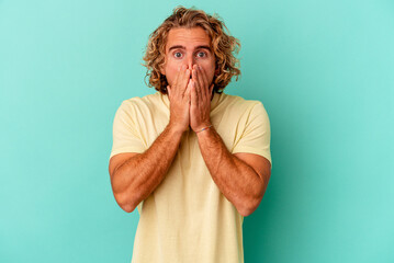 Wall Mural - Young caucasian man isolated on blue background shocked, covering mouth with hands, anxious to discover something new.