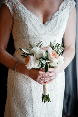 Wall Mural - Beautiful small wedding bouquet of flowers in hands of the Bride holding an elegant bouquet made of white peonies and greenery Cropped photo	