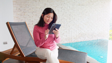 Canvas Print - Asian woman relaxing on a pool bed and using digital tablet near the private pool during her morning