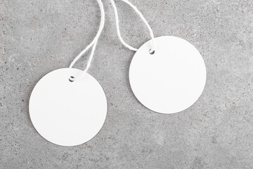 Two round white tag mockups with white cord, close up. Blank paper price tag isolated on grey stone background