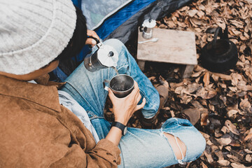 Asian lesbian sitting pouring hot water of espresso with Italian Moka coffee pot drinking in a forest on vacation, traveler outdoor the tent happy single picnic camping on the morning