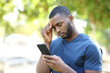 © PheelingsMedia - Worried man with black skin checking mobile phone in a park