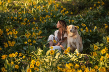 Female Sitting With Their Dog In A Field Of Wildflowers