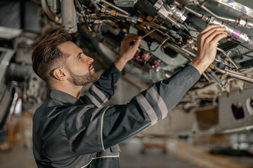 Bearded young man aviation mechanic checking aircraft components while working in repair station