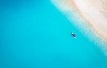 Aerial Top Down View Of A Woman On A Stand Up Paddle (SUP) Board Over Turquoise Sea Next To A Tropical Paradise Beach In The Bahamas