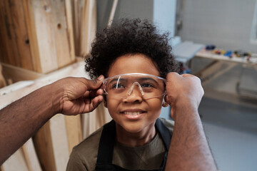 Wall Mural - Close up of unrecognizable African-American man giving protective goggles to cute son helping father in workshop