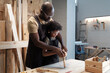 © pressmaster - Waist up portrait of caring African-American father teaching son in carpentry workshop, copy space