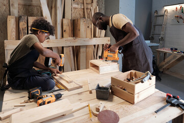 Wall Mural - Side view portrait of African-American father and son working in carpentry workshop together