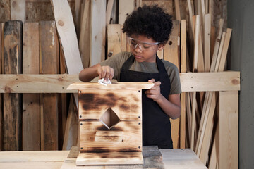 Wall Mural - Front view portrait of teenage African-American boy building wooden birdhouse in workshop, copy space