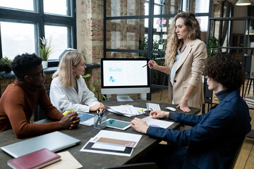 Aufkleber - Pregnant businesswoman pointing at computer monitor with financial graphs and talking to her colleagues during business presentation at office