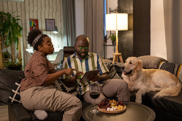 Wall Mural - African woman pointing at the screen of tablet pc and choosing the movie together with her boyfriend during their romantic evening at home