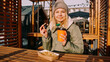 © brillianata - Woman eating tasty french fries and drinking tea or coffee in outdoor cafe. Woman at an urban outside street food court. Wooden decor and light bulbs