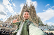 Happy tourist visiting La Sagrada Familia, Barcelona Spain - Smiling man taking a selfie outside on city street - Tourism and vacations concept