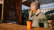 © brillianata - Happy woman on a winter sunny day at a street food fair in space for relaxing and meeting friends. She drinks coffee or mulled wine from an orange cup