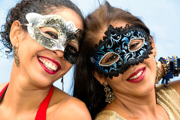 Close-up of face of two women wearing Venice Carnival mask against light background.