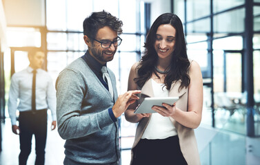 Poster - Working with twice the expertise. Shot of two businesspeople working on a digital tablet in a busy office.