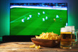Beer and snacks set on football match tv background