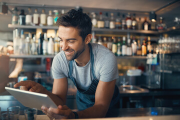 Poster - Streamlining small business tasks with smart tech. Shot of a young man using a digital tablet while working behind a bar counter.