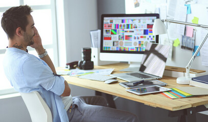 Poster - Portrait of young designer sitting at graphic studio in front of laptop and computer while working online.