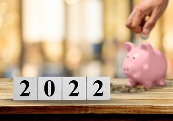 Poster - Text of 2022 number written on wooden blocks with blur of coins and pink piggy bank