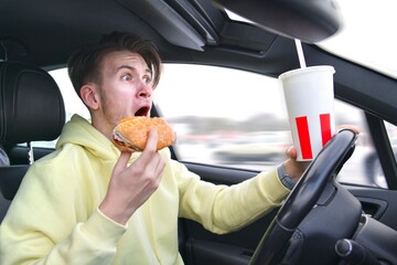 Careless Handsome frightened fearful guy driver young scared man screaming shocked about to have traffic accident driving car on road holding steering wheel of automobile eating burger drinking soda