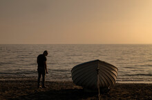 Silhouette Of Adult Man Standing On Beach With Fishing Boat During Sunset. Almeria, Spain