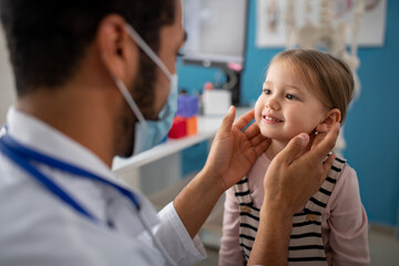 Wall Mural - young male doctor checking little girl's lymph nodes in his office.