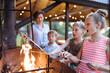 © Iryna - Middle age mother with three children cooking marshmallow candies on barbecue on the grill brazier at backyard. Children Preparing Delicious Marshmallows at Summer Evening.