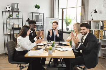 Wall Mural - Successful business colleagues applauding during conference meeting at modern boardroom. Multiracial partners feelings happiness while reaching common consensus.