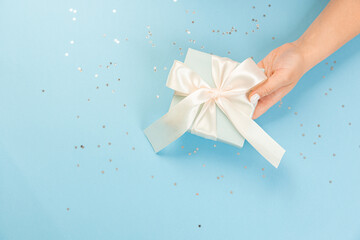 Wall Mural - A hand holds a blue gift box on a blue background with glitter stars. top view, copy space