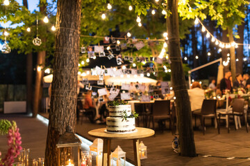 night wedding ceremony, the arch is decorated with flowers, candles and garlands of light bulbs and there is a wedding cake on the table