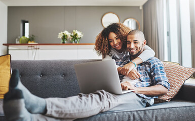 Wall Mural - Theres no denying their connection. Shot of a young woman hugging her husband while he uses a laptop on the sofa at home.