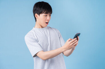 Young Asian man using smartphone on blue background