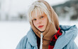 © bodnarphoto - Close photo of a beautiful lady with blond hair in warm clothes and a hood on a background of snowy city in winter, looking at the camera.