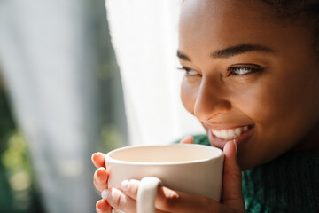 Young black woman with pigtails smiling while drinking tea