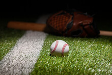 Low Angle View Of Baseball On Grass Field With Stripe And Defocused Mitt And Bat
