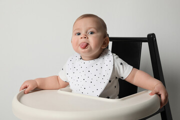 Poster - Cute little baby wearing bib in highchair on white background