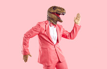 Funny Man In Rubber Dinosaur Mask Dancing And Having Fun In The Studio. Happy Lizard Headed Guy In Stylish Funky Vibrant Pink Party Suit Doing Egyptian Dance Moves Isolated On Pink Colour Background