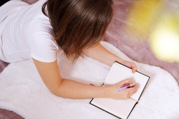 Poster - A closeup shot of a beautiful Caucasian woman laying on ground and writing in her notebook