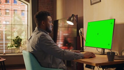 Poster - Young African American Man Working from Home on Desktop Computer with Green Screen Mock Up Display. Creative Male Checking Social Media, Browsing Internet. Urban City View from Big Window.