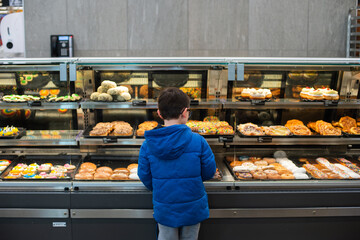 A boy stands in front of a donut case, trying to decide which to purchase