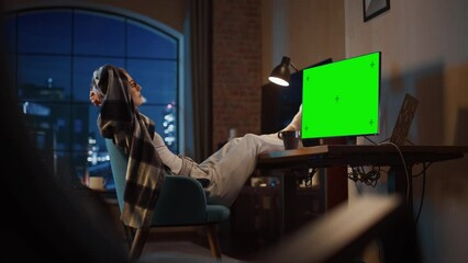 Aufkleber - Young Beautiful Female Streaming Videos at Home on Desktop Computer with Green Screen Mock Up Display. Creative Female Wearing Cozy Clothes, Resting Feet on Table and Enjoying Her Evening.