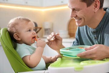 Father feeding his cute little baby in kitchen