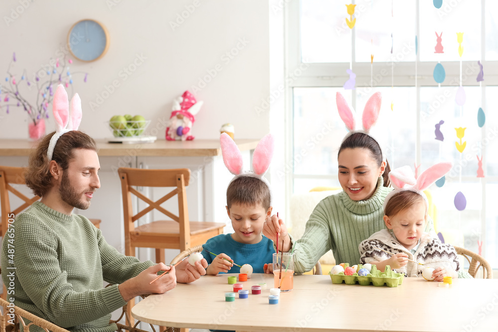 Happy family in bunny ears painting Easter eggs at table