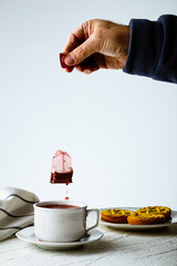 Sticker - A vertical shot of a person making tea with a teabag on the table with biscuits on it