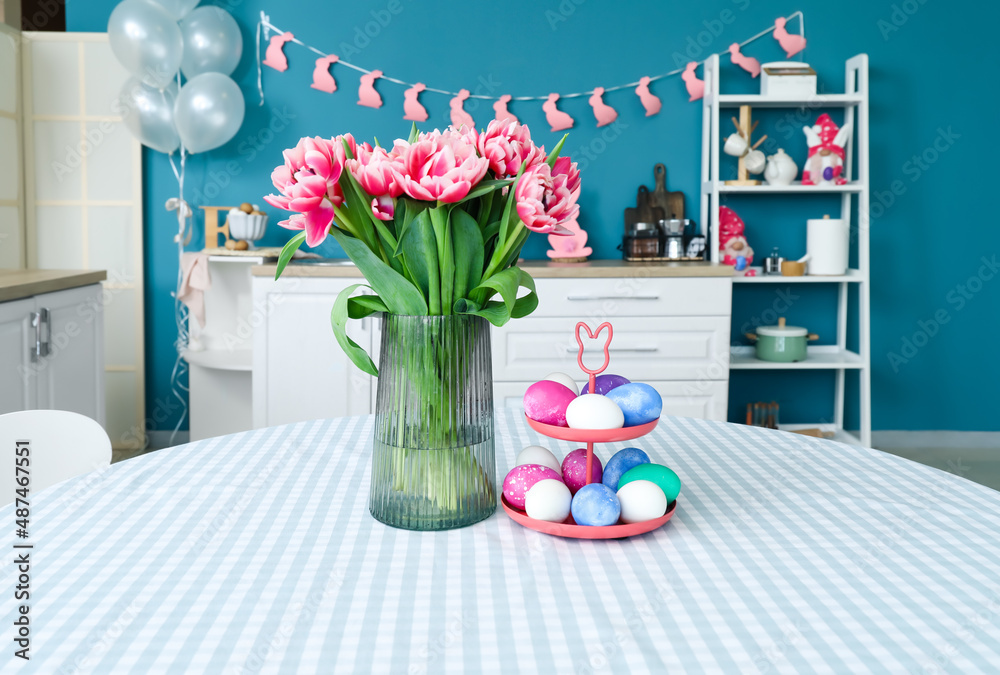 Stand with Easter eggs and vase with tulips on dining table
