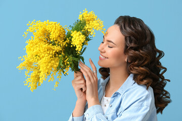 Wall Mural - Beautiful young woman with bouquet of mimosa flowers on blue background